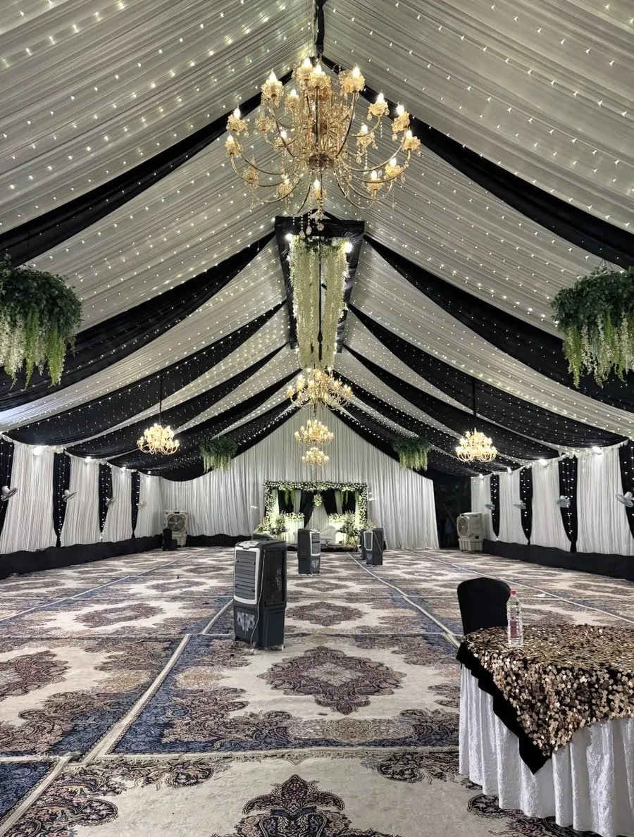 Large black and white draped tent with gold chandeliers, fairy lights, carpets and stage by Raju Tent & Catering Services, Bilaspur