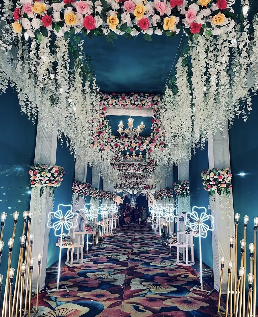 Entry passage with colourful flower frames, hanging white flowers and light-up flower stands by Raju Tent & Catering Services, Bilaspur