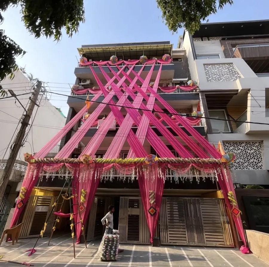 House front decorated with pink fabric drapes, flower garlands and umbrellas for a wedding by Raju Tent & Catering Services, Bilaspur