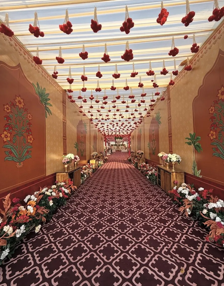 Rajasthani style painted entry passage with hanging red flower strings and carpet by Raju Tent & Catering Services, Bilaspur
