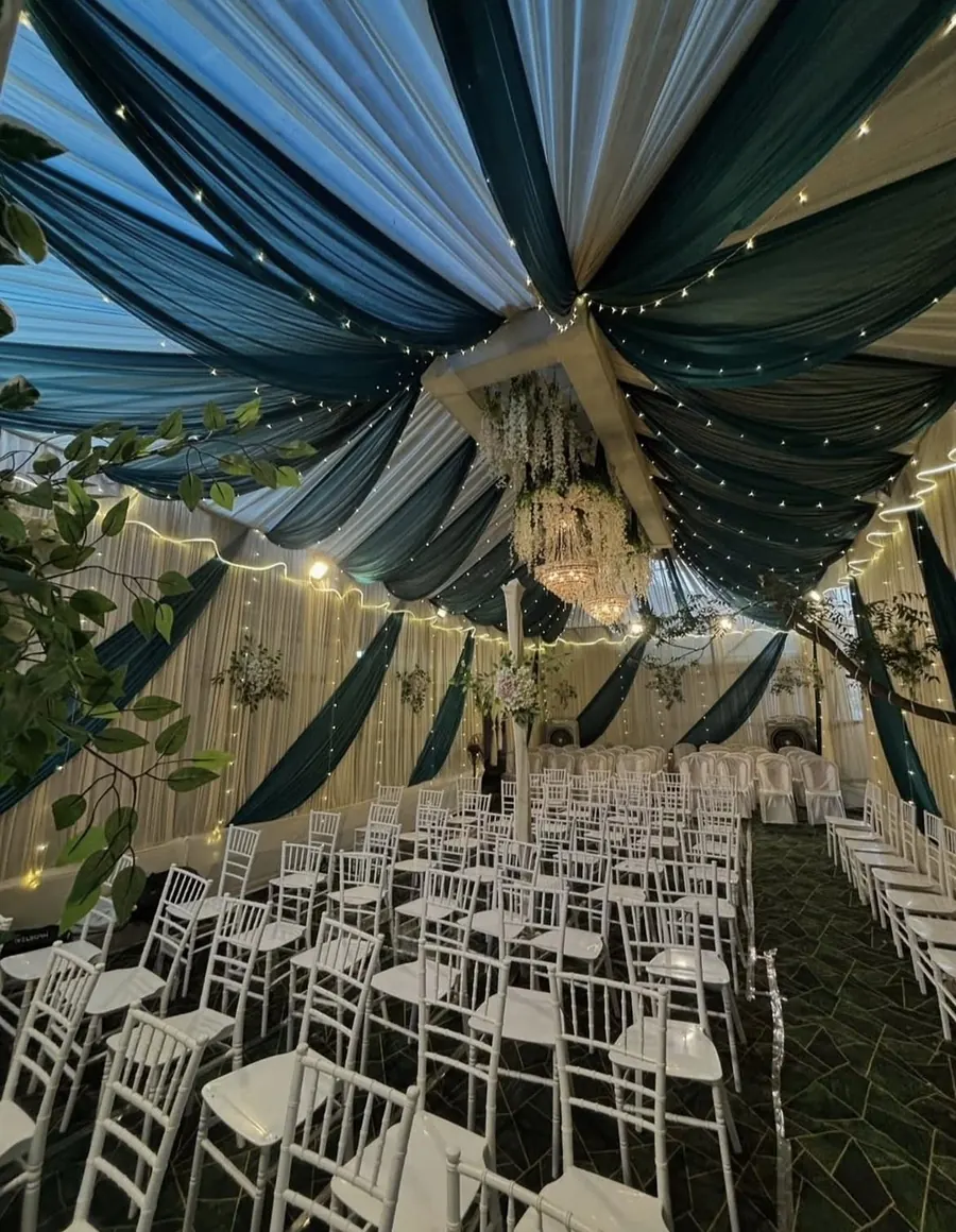 Tent with teal and white ceiling drapes, fairy lights, chandelier and rows of white chairs by Raju Tent & Catering Services, Bilaspur