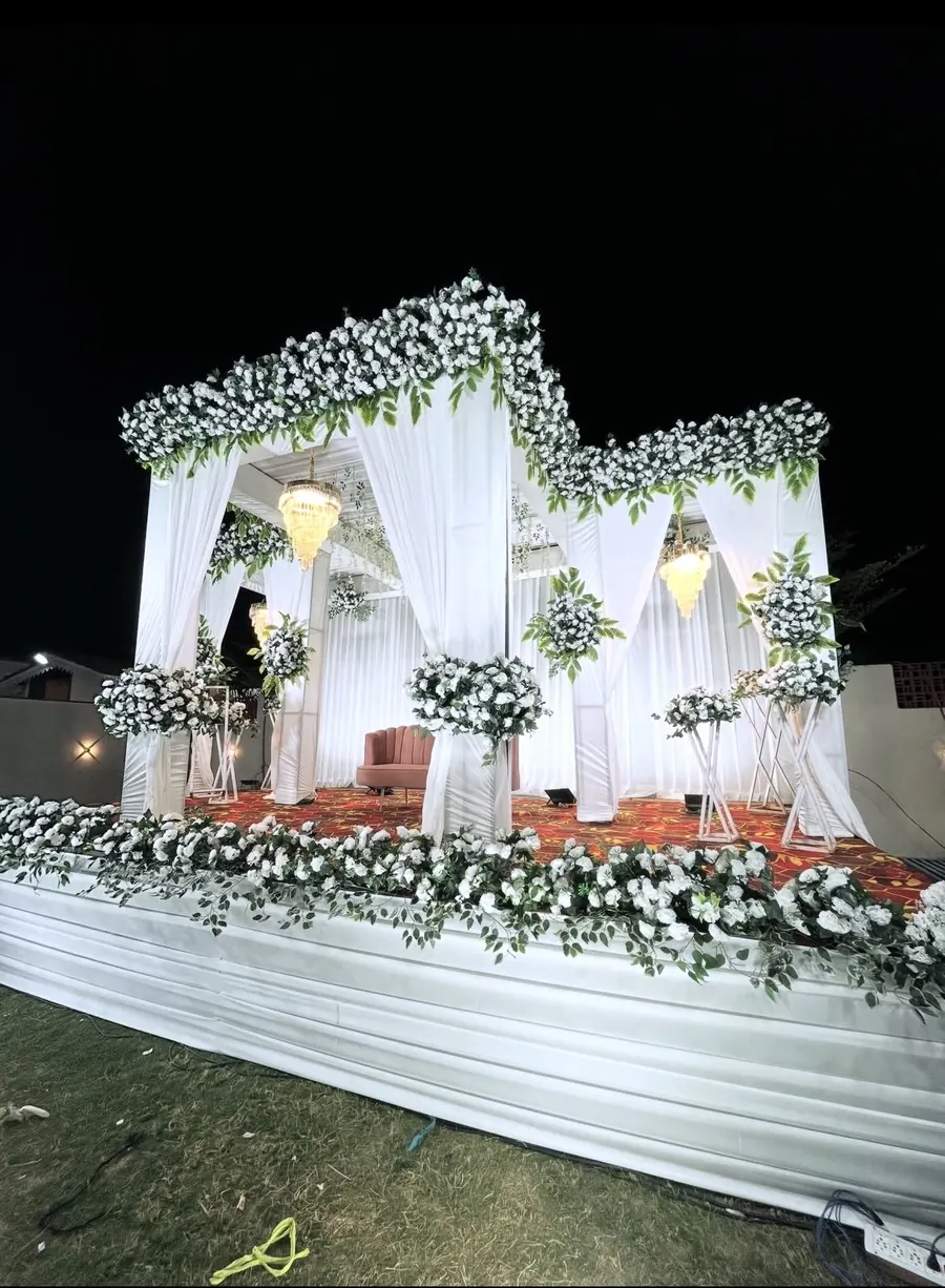 White draped wedding stage with chandeliers and white floral decoration on a lawn by Raju Tent & Catering Services, Bilaspur